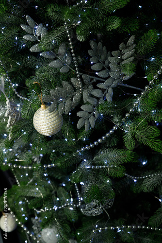 Closeup of green Christmas tree with white pearl bauble and silver glittery leaves Small LED lights glow among needles creating festive holiday atmosphere with dark background