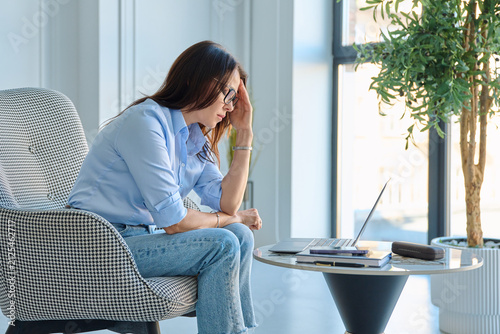 Mature woman suffering from menopause hot flashes wiping forehead at work in office