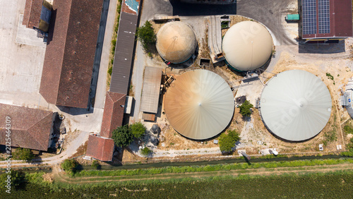 Aerial view of Cascina Antegnatica biogas plant with large circular digester tanks, farm buildings with tiled roofs, and solar panels in Tavazzano con Villavesco, Lombardia, Italy.