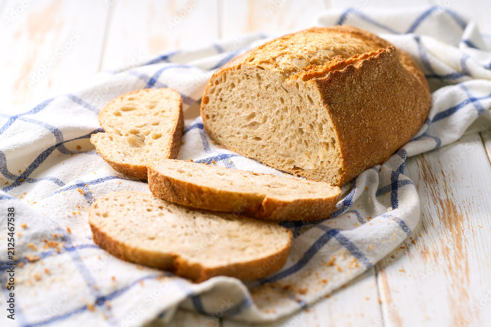Naklejka premium loaf of artisan bread or traditional wheat rustic bread on white kitchen table.