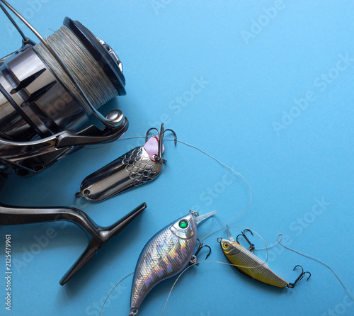 Foto Close‑up of a metallic fishing reel and three detailed lures on a light blue background