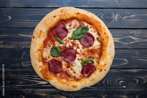 A round pepperoni pizza with cheese and basil sits on a wooden table.
