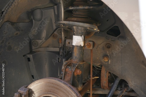 Fotografía Close-up of a worn suspension strut with rusty coil spring inside a vehicle wheel arch