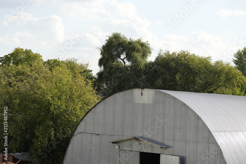Large industrial warehouse with curved metal roof surrounded by trees representing commercial architecture and storage infrastructure