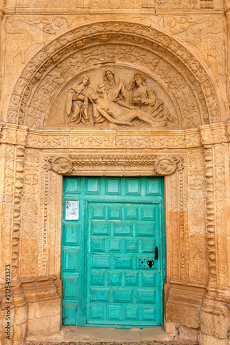 Obraz na plátně Plateresque south portal detail with turquoise wooden door & Lamentation of Christ stone tympanum