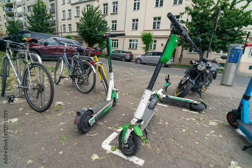 Several bicycles and electric scooters parked together. These modes of transportation are used for active travel on campuses and in cities. E-scooters, rental option in cities. To rent and park. 