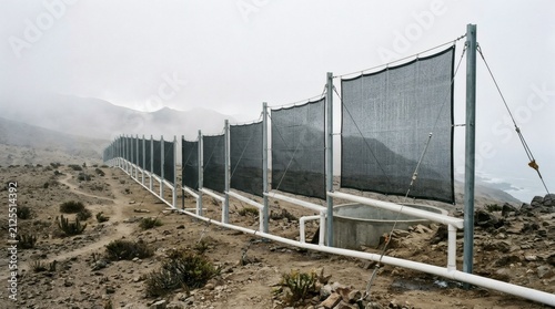 Shade netting structure on arid hillside overlooking ocean on foggy day