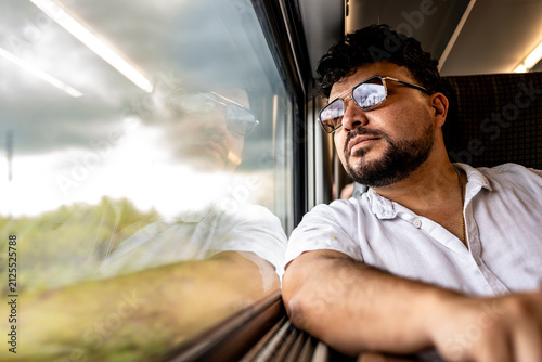 Thoughtful man traveling by train looks through the window during the journey, with wide copy space on the left, ideal for travel, lifestyle, transportation and advertising concepts.