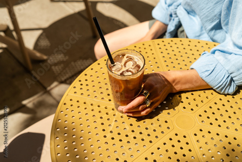 Close-up of a stylish Woman sitting at an outdoor cafe table holding an iced espresso tonic drink