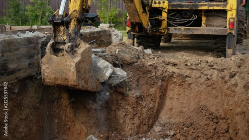 Fotografie Excavator bucket working to break up concrete and move soil, digging a deep tren