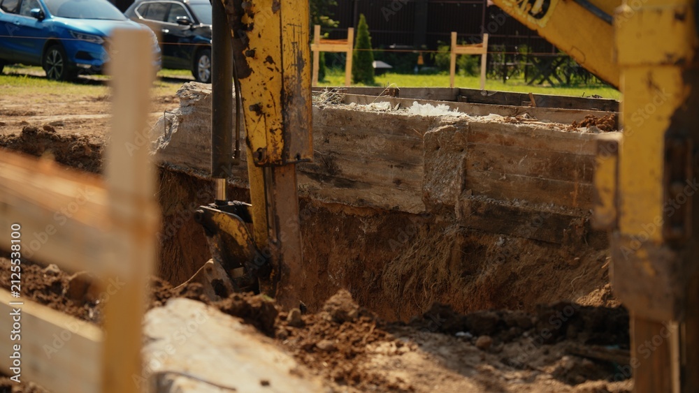 Fototapeta premium Excavator machine working on an earthwork project, digging a deep trench for new building foundation on a sunny day at a residential construction site