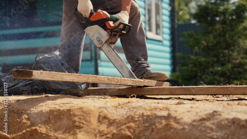 Obraz na plátne Worker wearing gloves using a power tool to saw a wood plank outdoors, creating