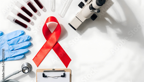 Red ribbon with blood samples, microscope, and clipboard for HIV AIDS awareness and research.