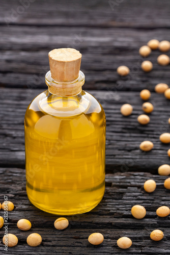 Golden soybean oil in a glass jar with a cork stopper and soybeans, stock photo with an aged wooden background and space for text.