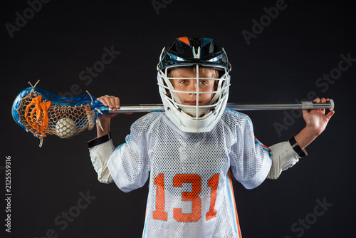 Youth lacrosse player in helmet holding stick across shoulders isolated on black background