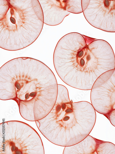 Translucent thin slices of red apples with visible seeds on a white background, creating a delicate and abstract pattern.