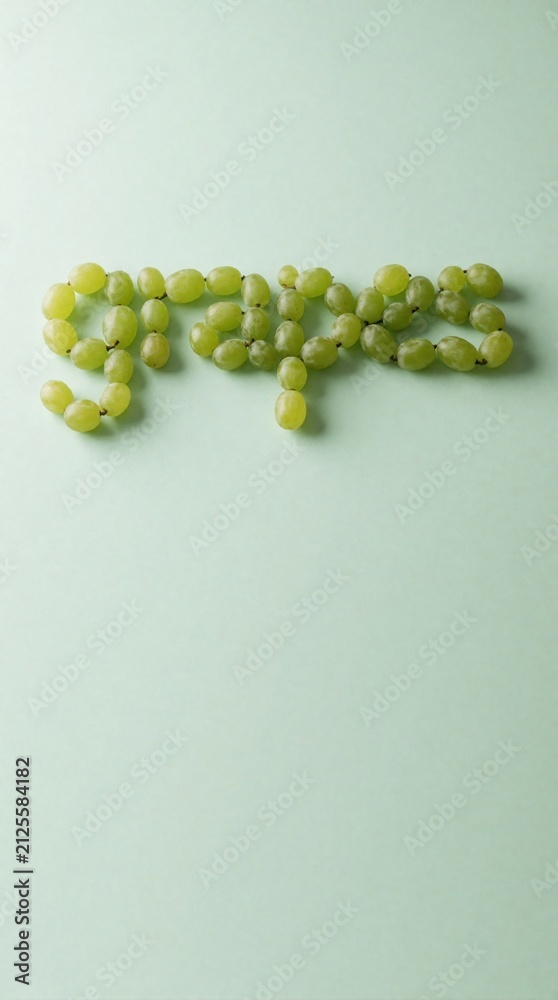 Obraz premium Green grapes arranged into word grapes spelling on pale green backdrop. Minimalist fruit art photography for creative design projects and food blogs.