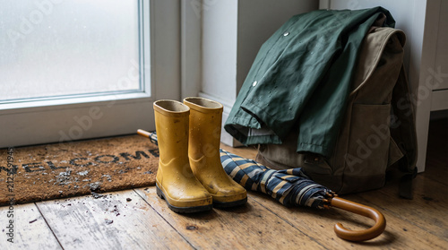 Wet yellow rain boots and umbrella on wooden floor