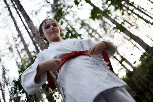 Photography Young girl tying a red belt in a karate gi outdoors in a forest during martial a