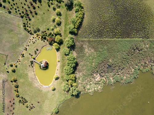 Aerial view of Salas Djordjevic featuring a small island with a gazebo in a pond surrounded by lush green meadows, trees, and wetlands in Palic, Vojvodina, Serbia.