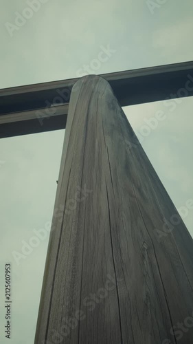 Low angle vertical close-up shot of a massive traditional wooden pillar and crossbeam of a Japanese Torii gate against an overcast sky