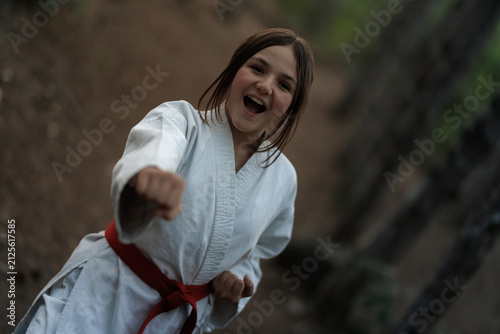 Konstfotografi Happy girl practicing karate punch outdoors in a forest wearing a white gi and r