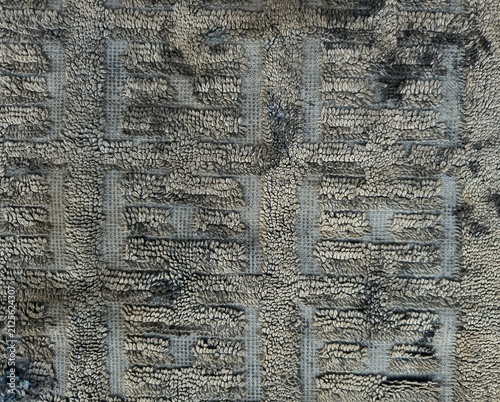 Close-up texture of a worn-out carpet with a geometric grid pattern showing dirt and stains.