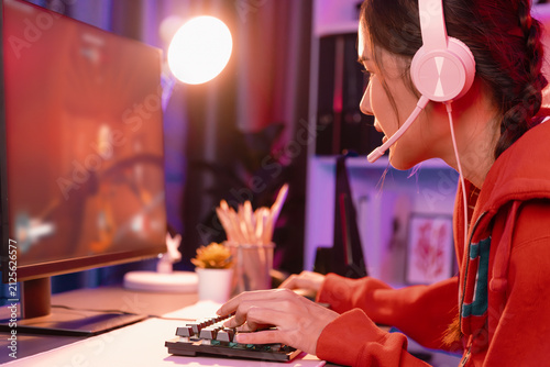 Photography Host channel of young beautiful Asian gaming streamer, playing battle team gaming with multiplayer or single at warship on screen, wearing pastel color headset at digital neon light room