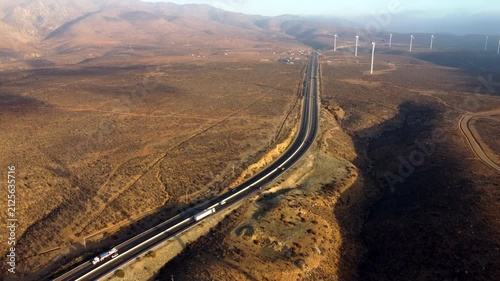 Aerial drone view of desert highway with wind turbines and traffic