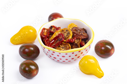 Фотография Vibrant dried tomatoes of different varieties (pear-shaped, chocolate sprinkle) with herbs and spices in olive oil are in the little ceramic bowl, fresh loose tomatoes are around