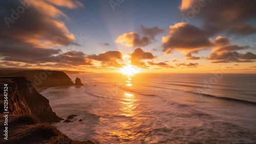 Golden sunset over coastal cliffs and reflective ocean shoreline at dusk.