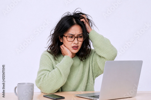 Asian woman with dark hair, looking tired checking her business report in the laptop