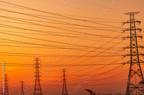 High voltage electricity transmission towers and power lines silhouetted against sunset sky. Electrical grid infrastructure, energy distribution, utility engineering and modern power networks.