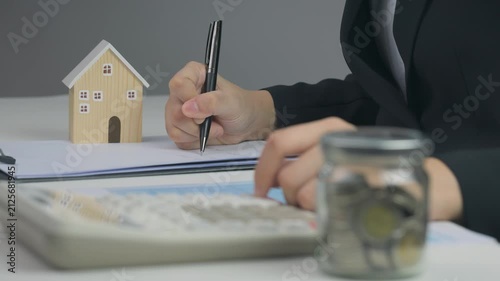 Focused person plans mortgage budget, calculates saving, signs paper, achieving lifelong home ownership goal near wooden house model