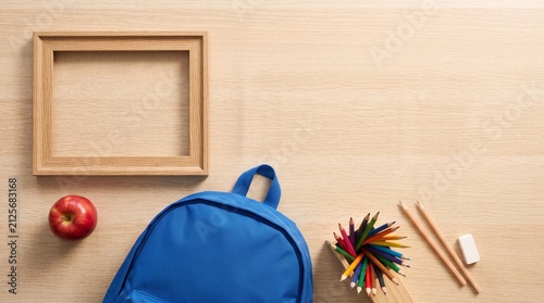 Back to school flat lay with blue backpack apple colored pencils and blank wooden frame on desk