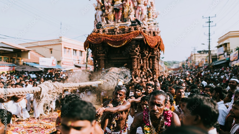 Obraz premium Towering wooden temple chariot pulled by devotees with heavy ropes during a dusty religious festival for cultural tradition and travel concepts