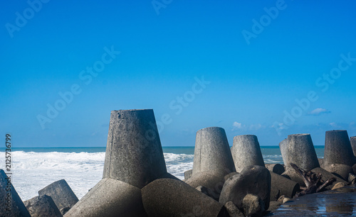 Фотография Concrete tetrapod breakwater protecting the shoreline from strong ocean waves under a clear blue sky