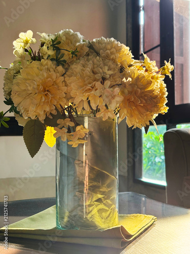 Photography Elegant yellow flower bouquet in a clear glass vase on a table, illuminated by warm sunlight from a window