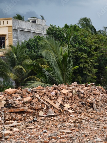 Pile of rubble from a demolished brick building with tropical palm trees in daylight