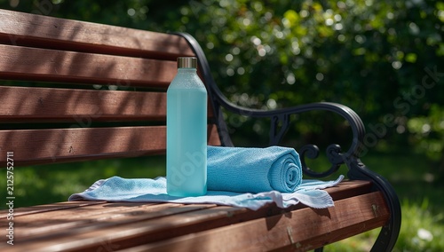 Blue water bottle and rolled towel on a wooden park bench