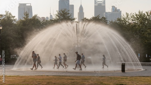 People walking through a large circular fountain in a city park