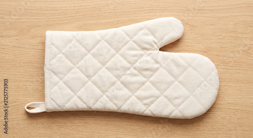 Single cream colored quilted oven mitt with a small loop for hanging on a light wooden background flat lay top view