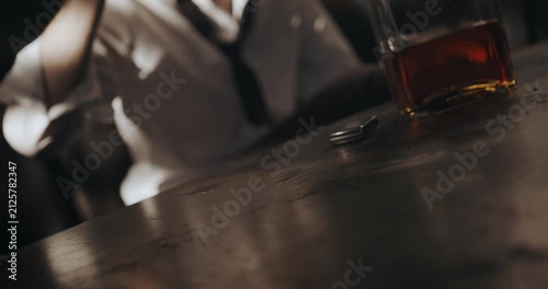 Whiskey glass slides across the table toward a seated man who catches it and takes a drink.