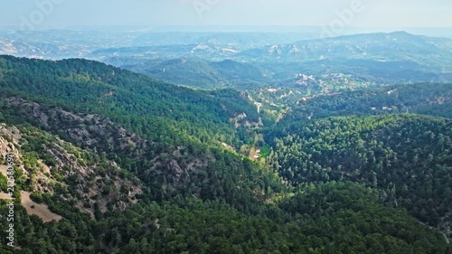 Drone view from Mount Olympus in Cyprus. Green valleys, forested hills and distant mountain ranges create a wide panoramic nature scene.