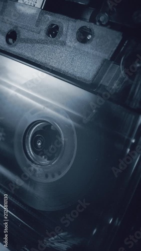 Vertical macro shot of a compact cassette hub spinning inside a tape deck. Close up of magnetic tape, transparent shell and reel motion in retro analog audio equipment