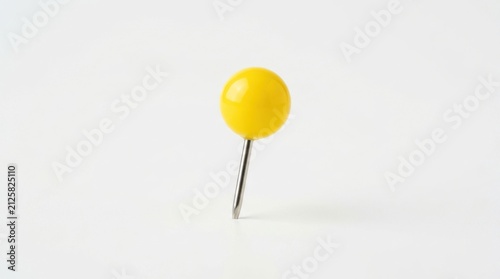 A single bright yellow push pin standing upright on a clean plain surface