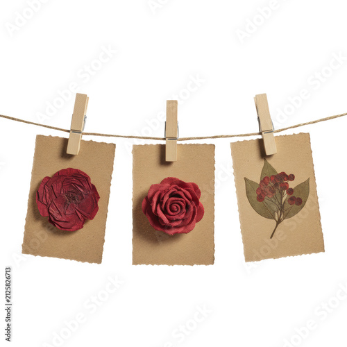 Three textured red flower shapes on torn kraft paper cards hanging from jute twine with wooden clothespins against white. handcrafted romantic atmosphere