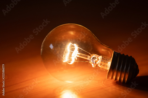 Quadro su tela One turned on incandescent light bulb glows brightly on a wooden table