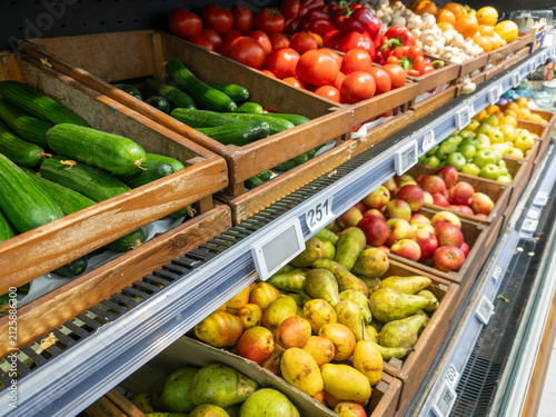 Fresh vegetables and fruits on supermarket shelves. Wooden crates with cucumbers, tomatoes, apples, and pears, symbolizing healthy nutrition and natural freshness