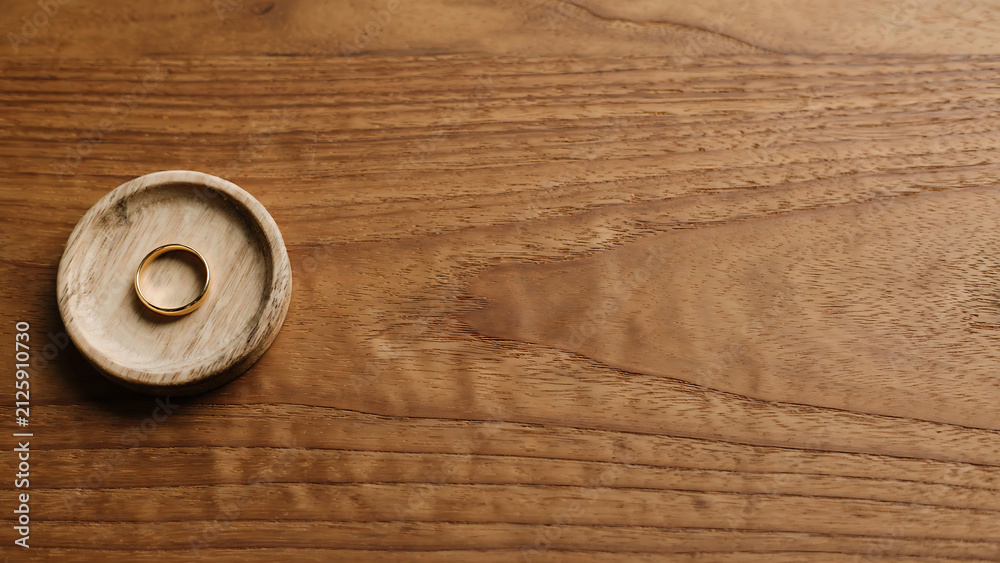 Fototapeta premium Minimalist gold wedding band on small wooden tray resting on timber table surface with ample copy space